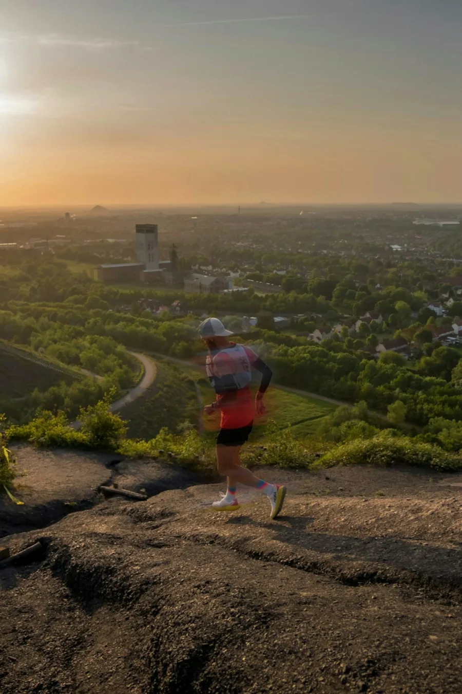 Läufer auf einem felsigen Weg mit Blick über eine grüne Landschaft